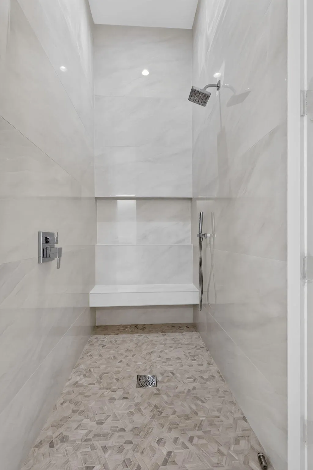 Walk-in shower with large format wall tiling, mosaic floor tiling, built-in bench, and a rainfall shower head with handheld spray