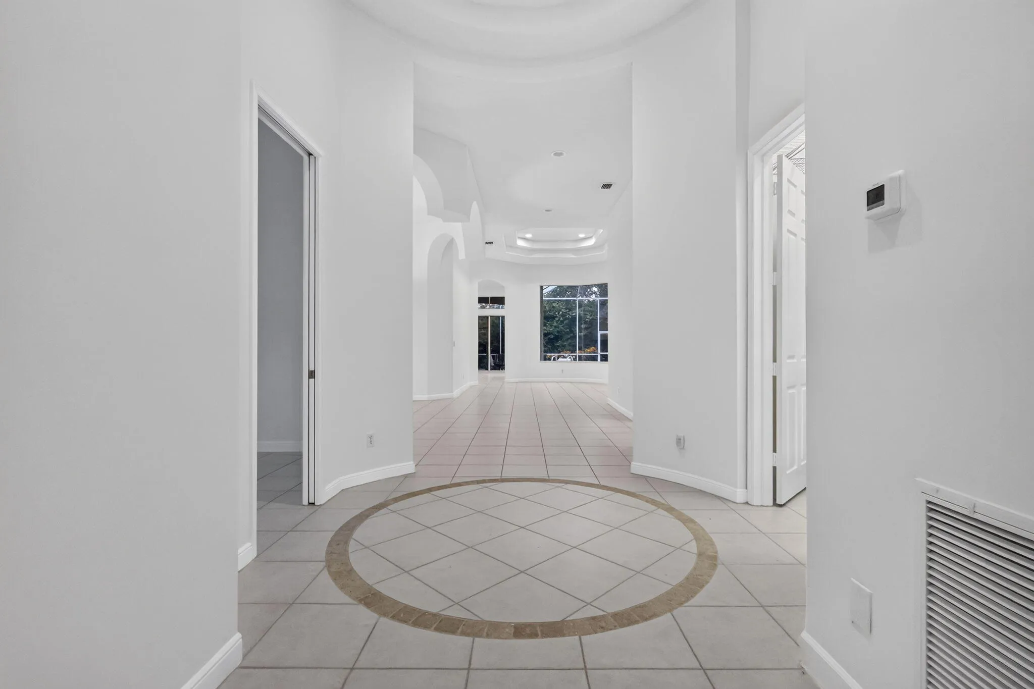 Tiled flooring with a circular inlay, arched doorways, tray ceilings, and a light-filled interior