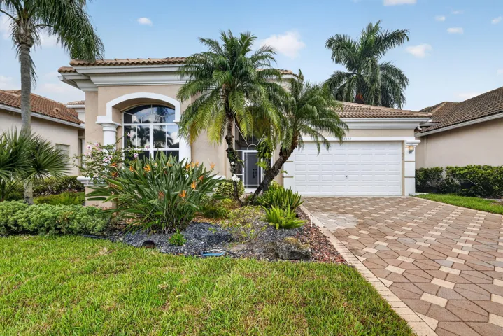 Stucco exterior with a tile roof, arched window, attached two-car garage, and a paver driveway