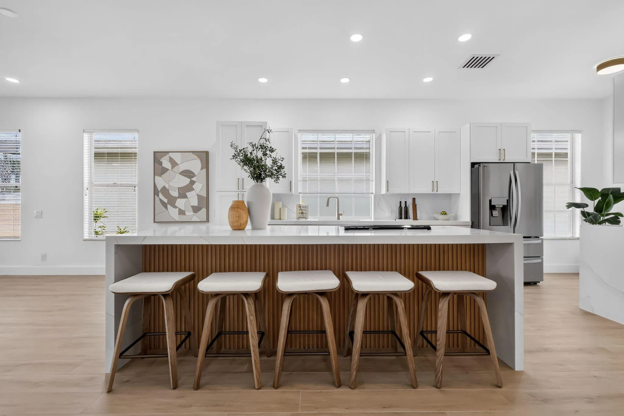 Open-concept kitchen featuring an island with wood-finish paneling, light wood-finish flooring, white cabinetry, and stainless steel appliances