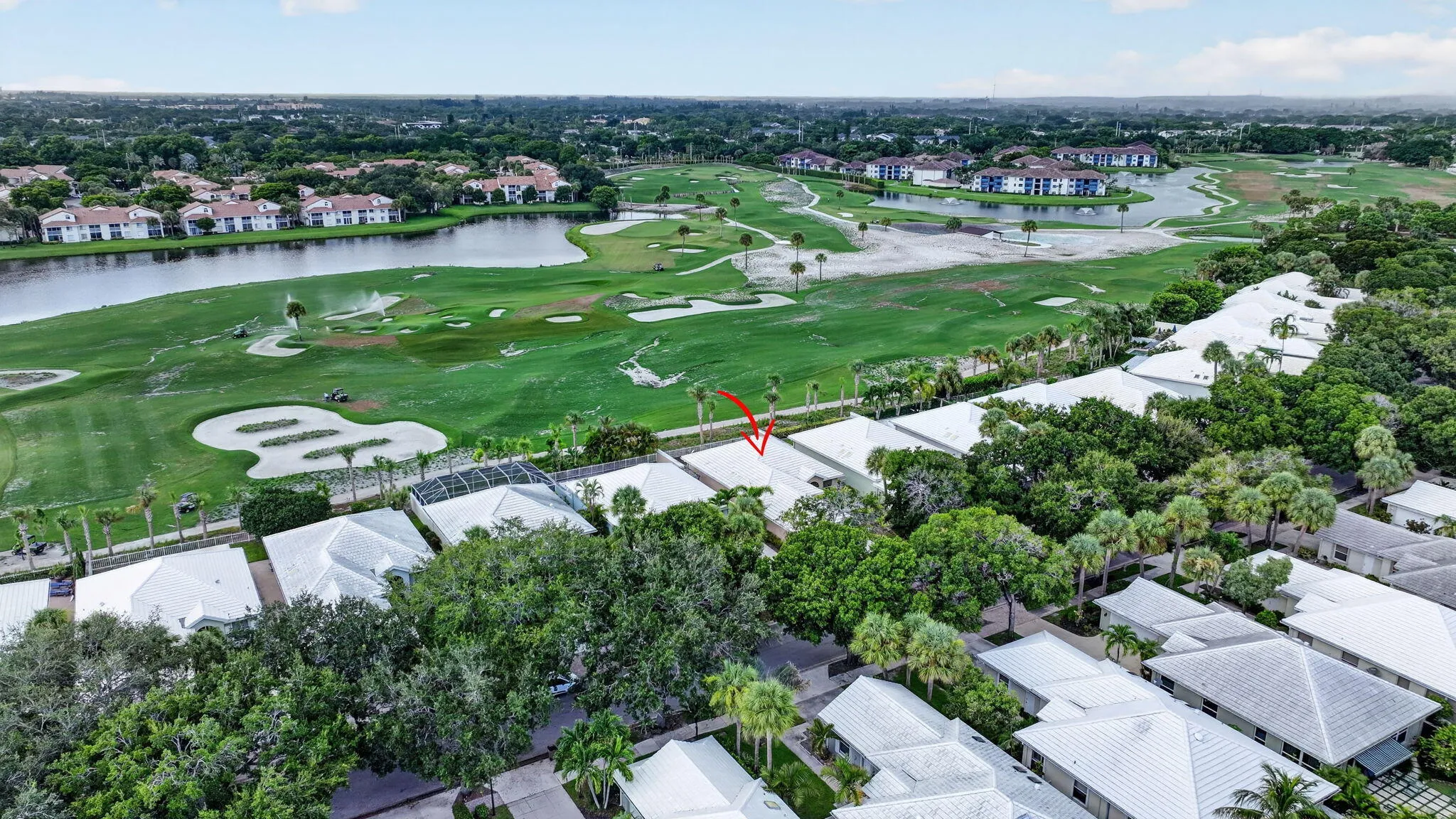 Aerial perspective showcasing a residential property with surrounding mature trees, a golf course, and a nearby body of water