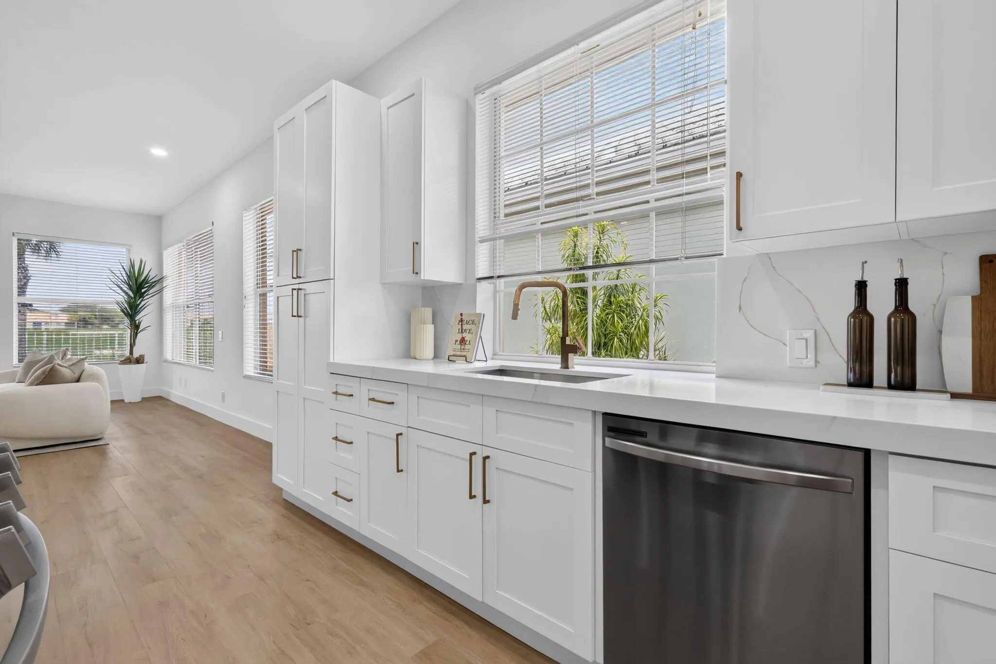 White shaker cabinetry, stainless steel dishwasher, wood-finish flooring, white countertops, and a full-height backsplash
