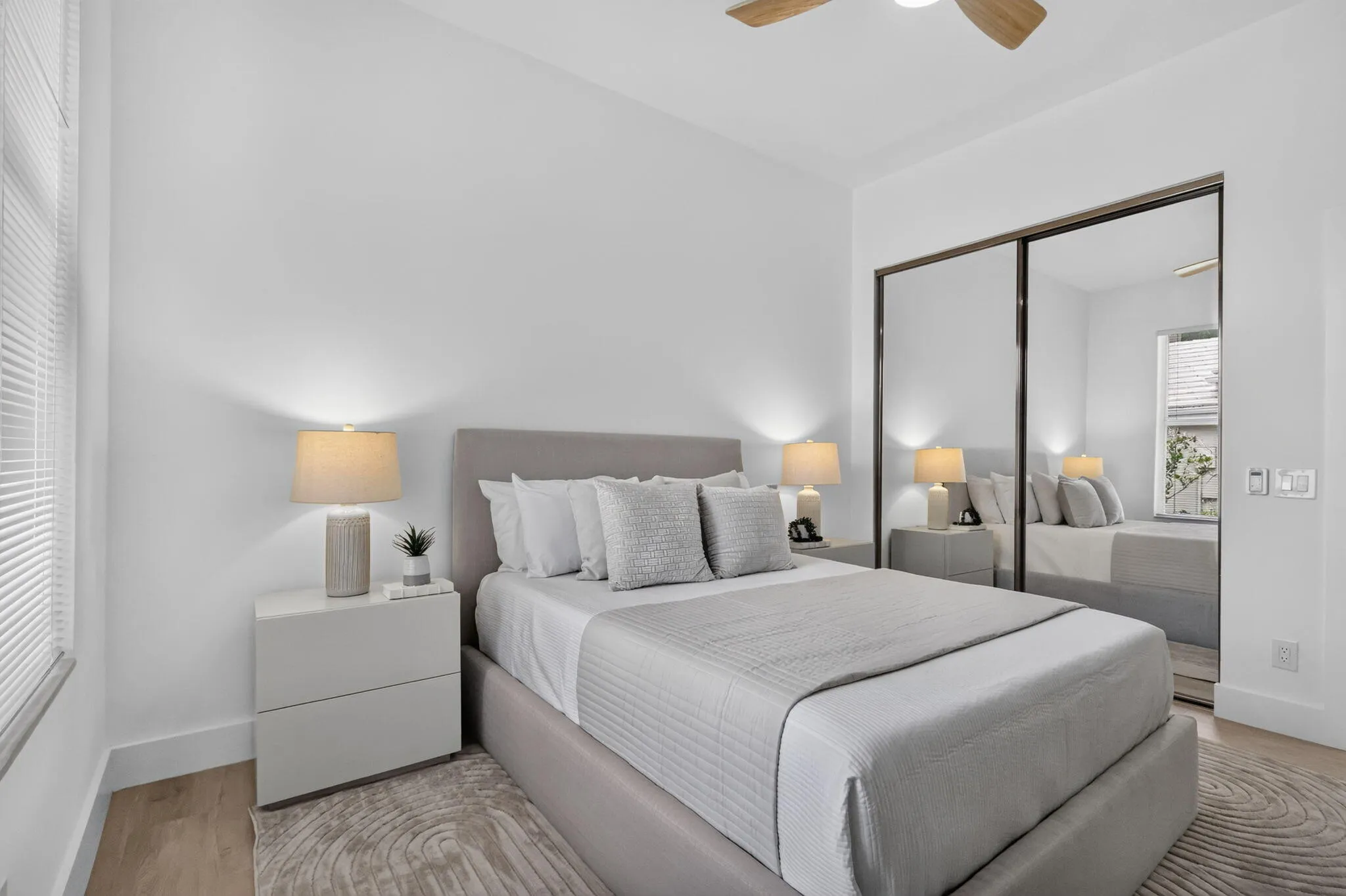 Light wood-finish flooring, mirrored closet doors, a ceiling fan, and white window blinds