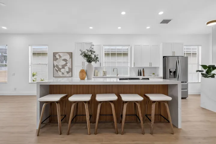 Open-concept kitchen featuring an island with wood-finish paneling, light wood-finish flooring, white cabinetry, and stainless steel appliances