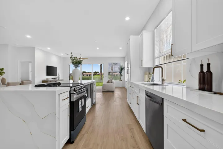 Open-concept kitchen featuring white cabinetry, light wood-finish flooring, and a large island with a cooktop
