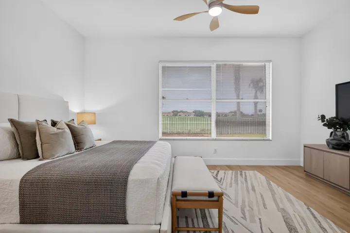 Spacious room featuring wood-finish flooring, a contemporary ceiling fan, and large windows with horizontal blinds