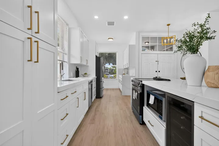 Bright kitchen with expansive white cabinetry, gold-finish hardware, wood-finish flooring, a built-in microwave, and a beverage cooler