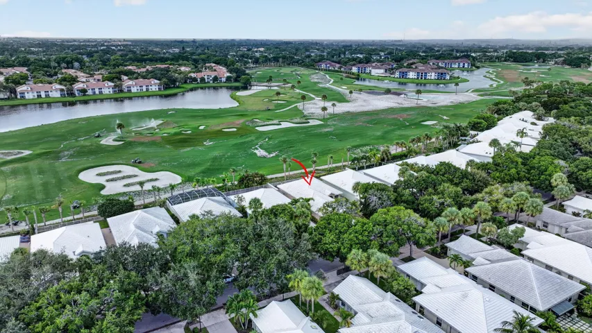 Aerial perspective showcasing a residential property with surrounding mature trees, a golf course, and a nearby body of water