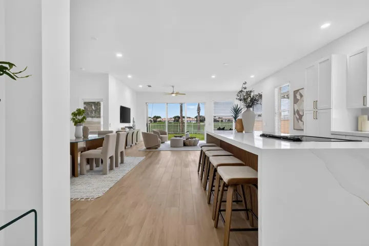 Spacious open-concept living area featuring wood-finish flooring, a kitchen island with seating, white cabinetry, and sliding glass doors to the exterior