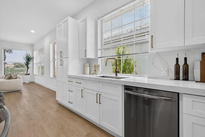 White shaker cabinetry, stainless steel dishwasher, wood-finish flooring, white countertops, and a full-height backsplash