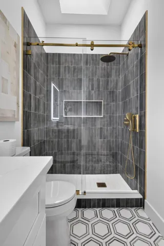 Walk-in shower with dark tile surround, gold-finish fixtures, and a glass enclosure