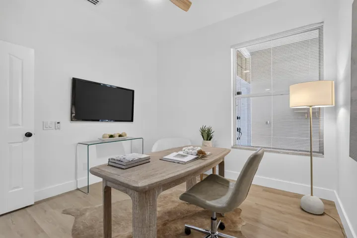 Wood-finish flooring, white paneled door with black hardware, wall-mounted television, and a window with horizontal blinds