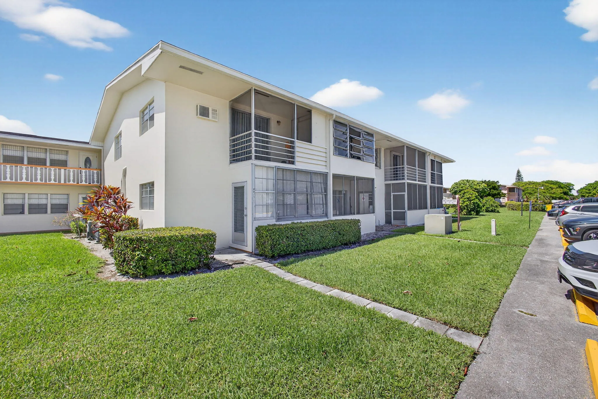 Two-story stucco building with screened-in balconies, aluminum railings, and mature landscaping