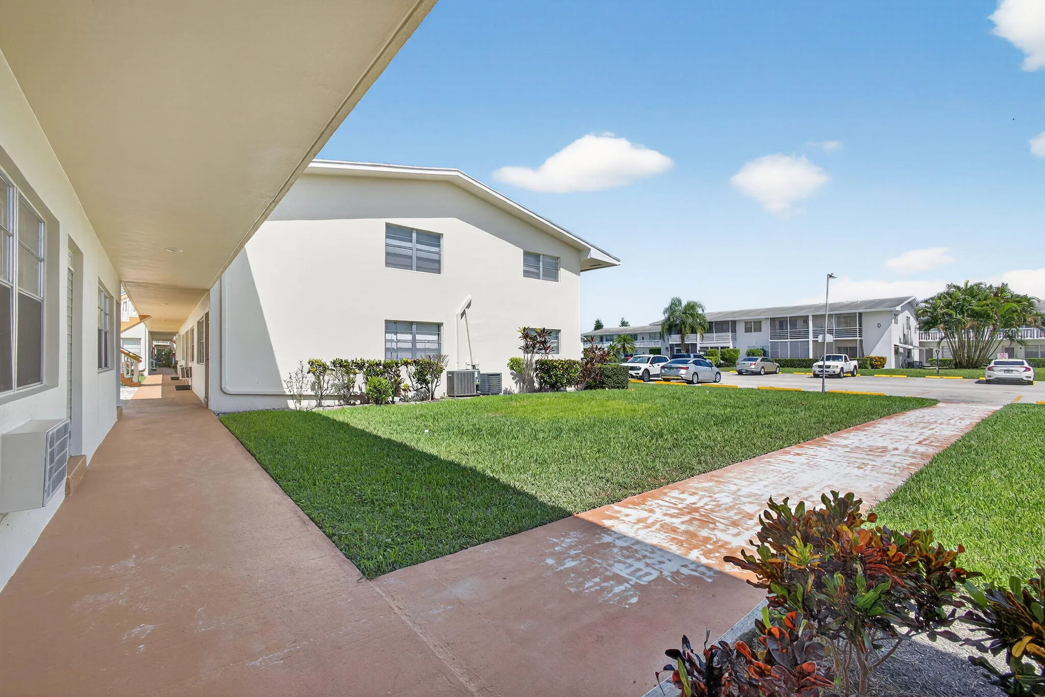 Exterior walkway with a covered patio, adjacent green space, and a building with multiple window units