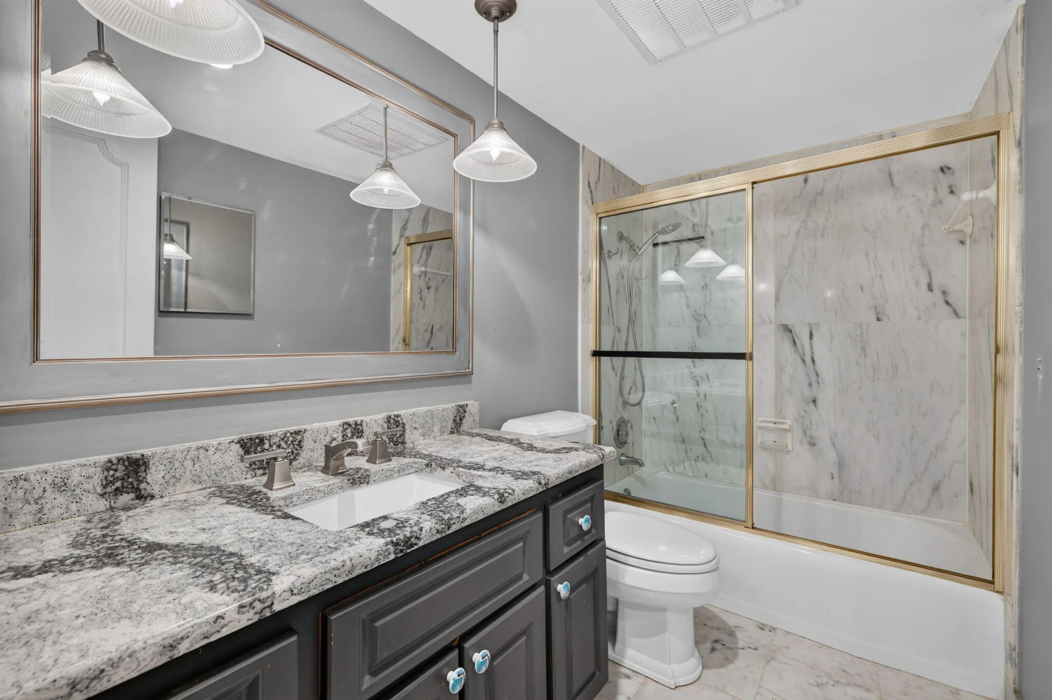 Granite countertop with integrated sink, dark wood-finish vanity, large framed mirror, glass-enclosed shower with tiled walls, and recessed ceiling lighting