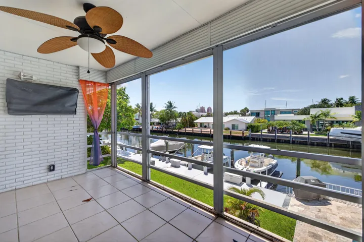 Screened outdoor area with tile flooring, white brick wall, and a woven ceiling fan