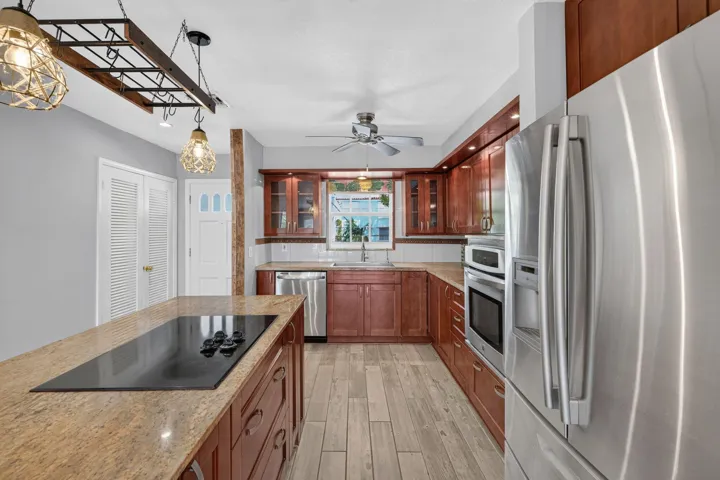 Galley kitchen featuring rich wood cabinetry with glass-front upper units, stainless steel appliances including dual wall ovens, granite countertops, wood-finish flooring, and pendant lighting with decorative shades
