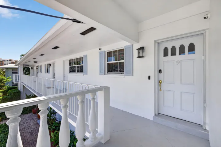 Exterior corridor access with white balustrade railing, light blue window shutters, and a paneled entry door with decorative glass inserts