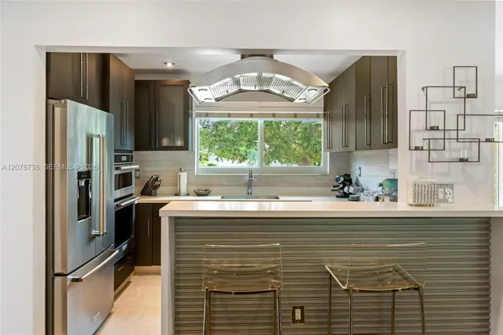 Dark cabinetry contrasts against bright countertops and stainless-steel appliances, while the open breakfast bar connects the kitchen directly to the dining and living areas.