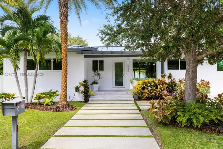 A modern metal roof, crisp white exterior, oversized stepping-stone driveway and lush greenery create a contemporary first impression without losing the warmth of a true neighborhood home.