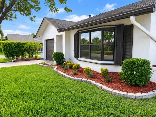 Single-story residence featuring a stucco exterior, a dark-toned bay window, louvered shutters, an attached garage, and stone-bordered landscaping beds