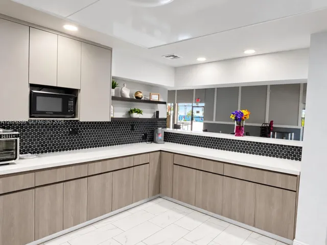 Contemporary kitchen featuring wood-finish cabinetry, white solid-surface countertops, black circular-tiled backsplash, recessed ceiling lighting, and tile flooring