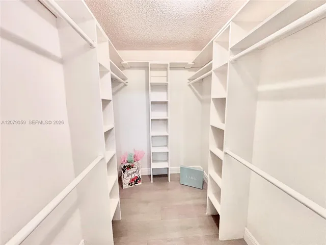 Primary bedroom spacious Walk-in closet featuring white built-in shelving, vertical storage towers, and vinyl waterproof wood-finish flooring. Lots of room for shoes, handbags and clothing.