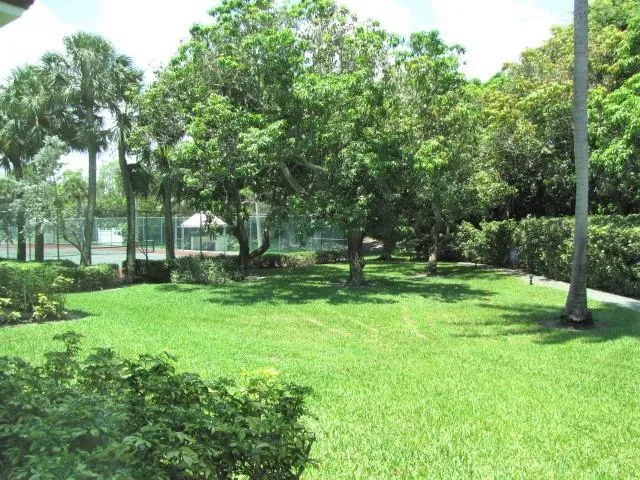 Expansive lawn with mature trees, established hedges, and a visible tennis court