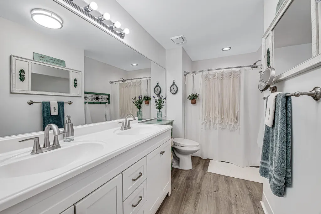 Dual sink vanity with white cabinetry, wood-finish flooring, and brushed nickel fixtures