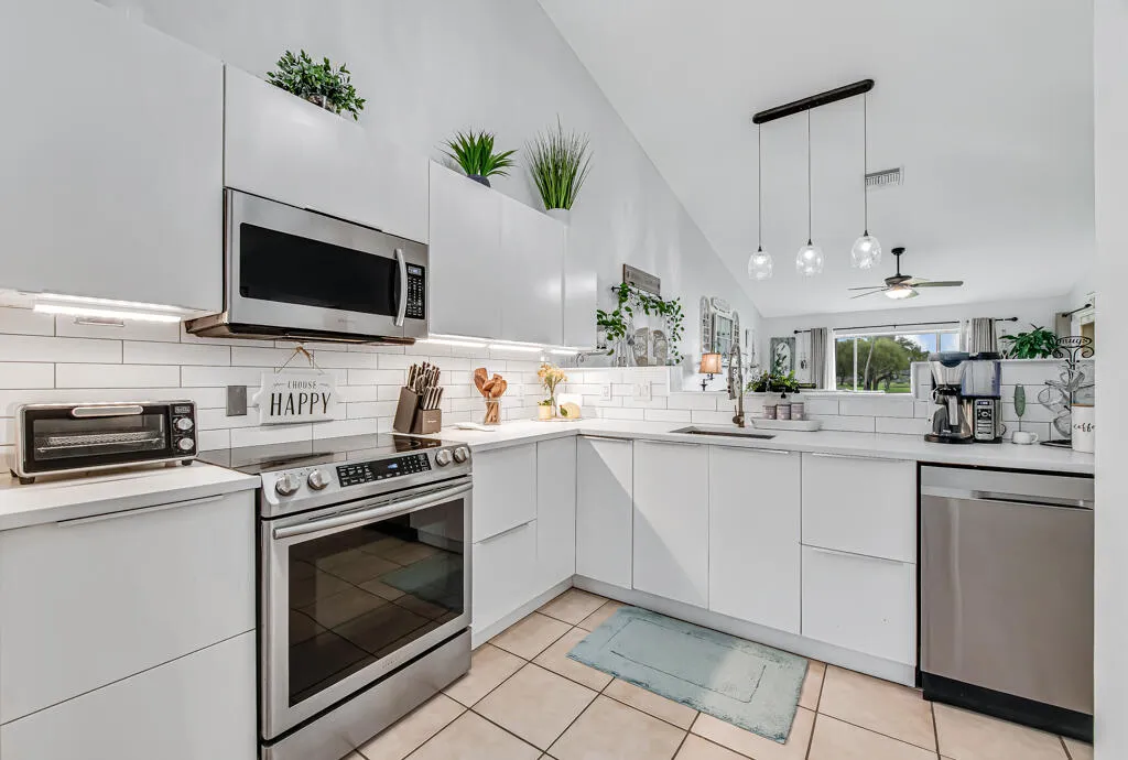 Modern kitchen featuring white flat-panel cabinetry, stainless steel appliances, a white subway tile backsplash, and light-toned countertop surfaces