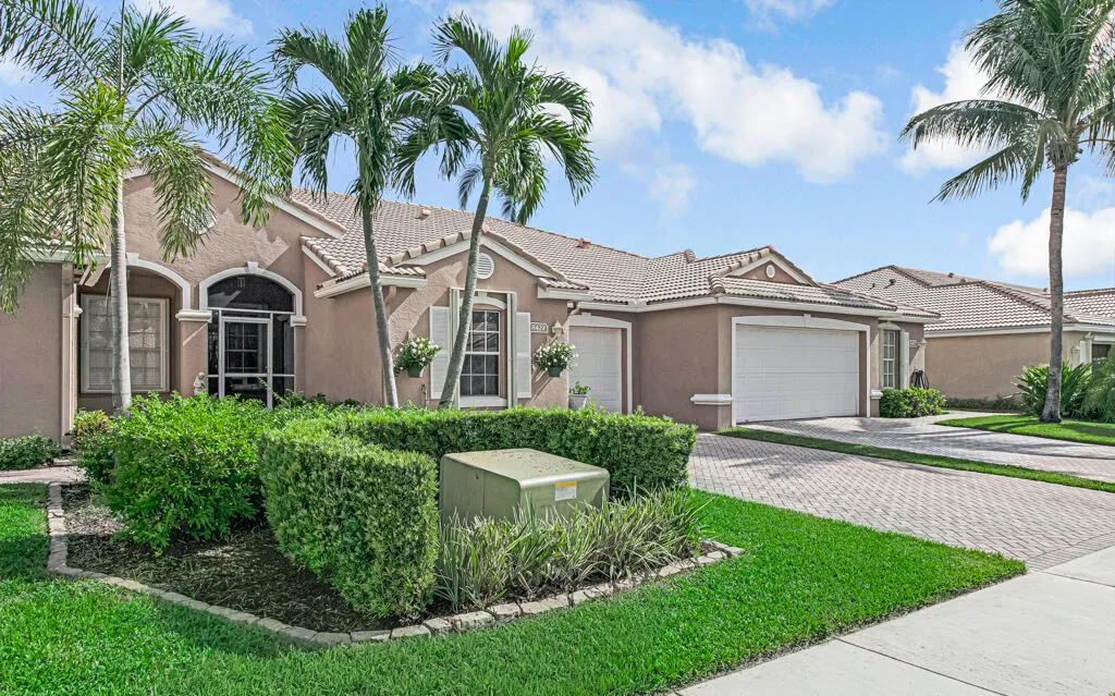 Stucco exterior with a tiled roof, screened front entry, decorative window shutters, and a paver driveway