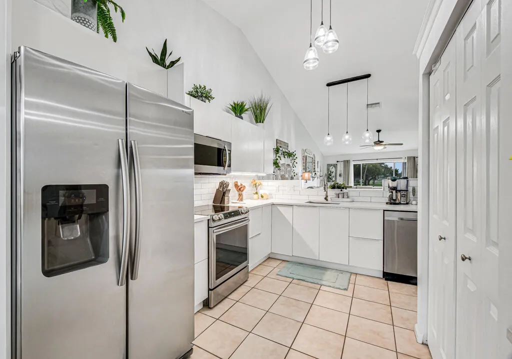 Vaulted ceiling kitchen featuring stainless steel appliances, white flat-panel cabinetry, a subway tile backsplash, and ceramic tile flooring