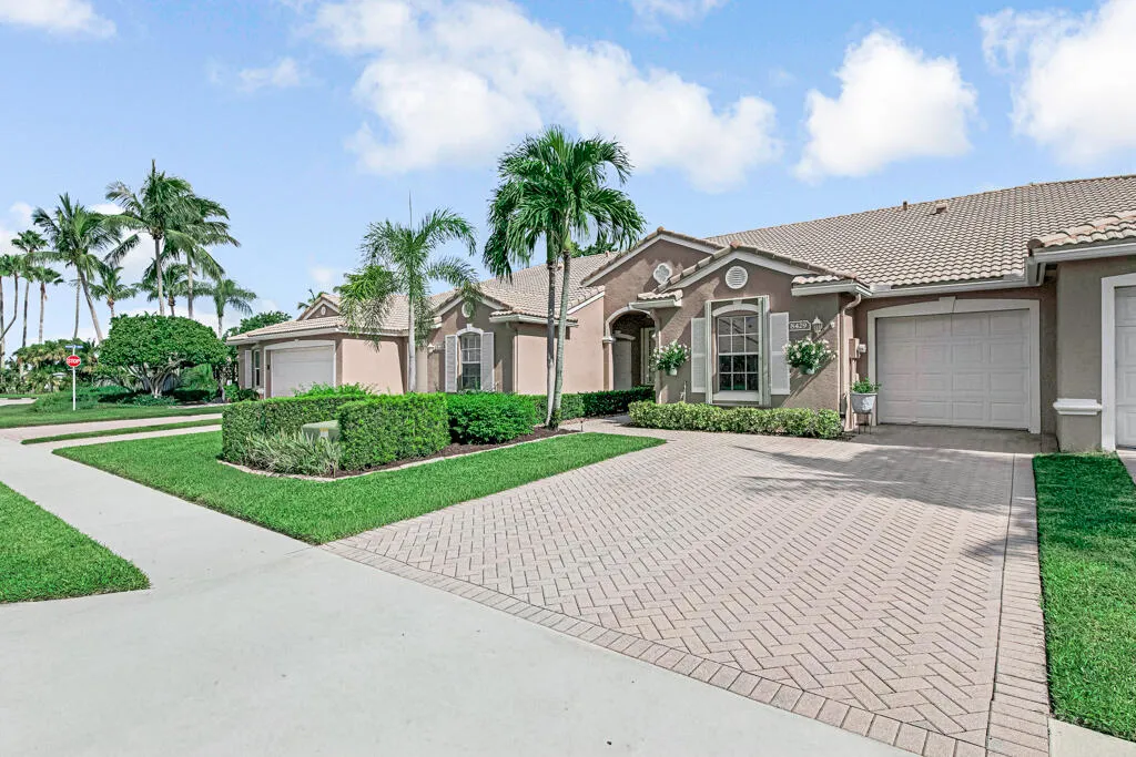 Neutral-toned exterior with a tile roof, decorative shutters, a paver driveway, an attached garage, and mature landscaping