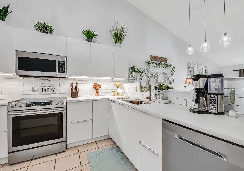 White flat-panel cabinetry, stainless steel appliances, white subway tile backsplash, white countertops, and vaulted ceilings