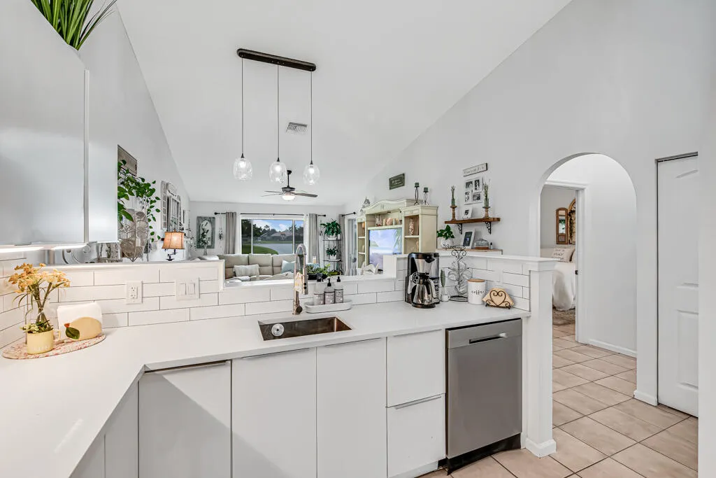 White cabinetry with integrated sink, subway tile backsplash, and stainless steel dishwasher