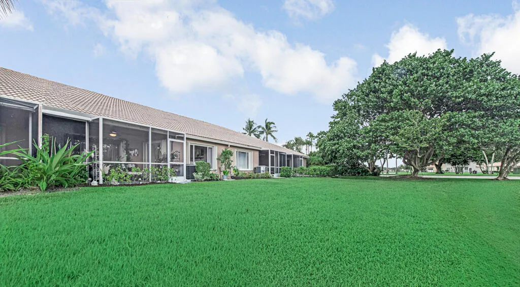 Expansive green lawn with mature trees and a tiled roof structure featuring multiple screened-in patios