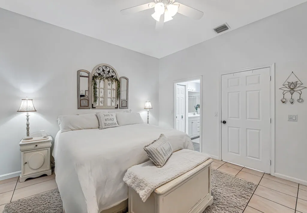 Vaulted ceiling, ceiling fan, tile flooring, interior panel doors, and an en-suite bathroom with a vanity and mirror