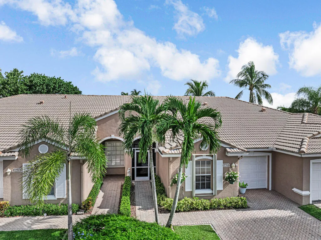 Exterior with a tiled roof, stucco finish, paver driveway, lush landscaping, and white garage doors