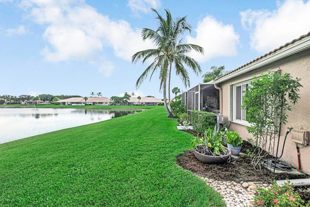 Lakeside property featuring a screened enclosure, mature landscaping, and an expansive lawn