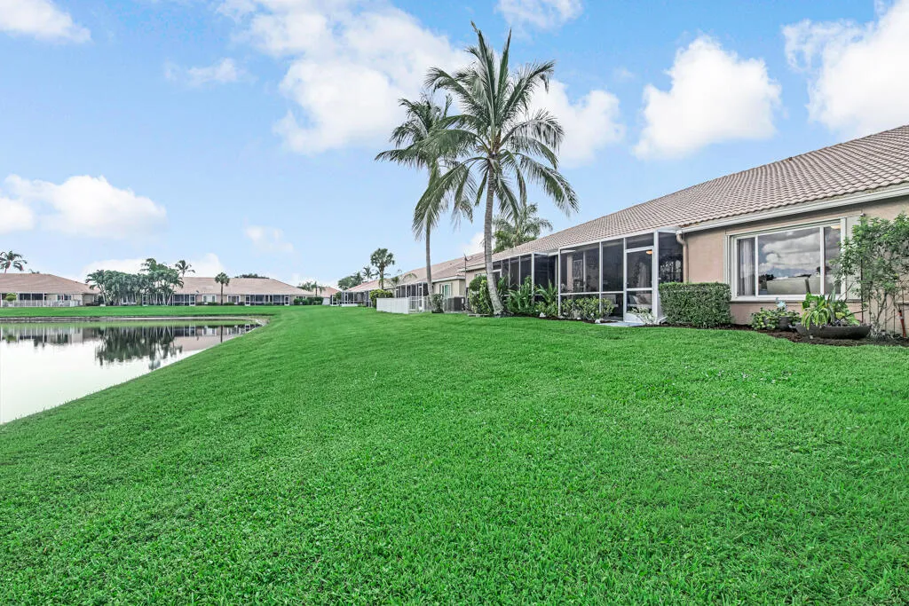 Expansive green lawn bordering a tranquil body of water, with mature palm trees and screened patio enclosures