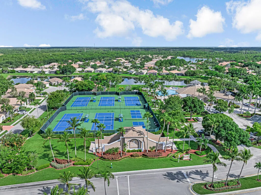 Community amenities featuring multiple tennis courts, a clubhouse, and a swimming pool, surrounded by mature palm trees and lush landscaping