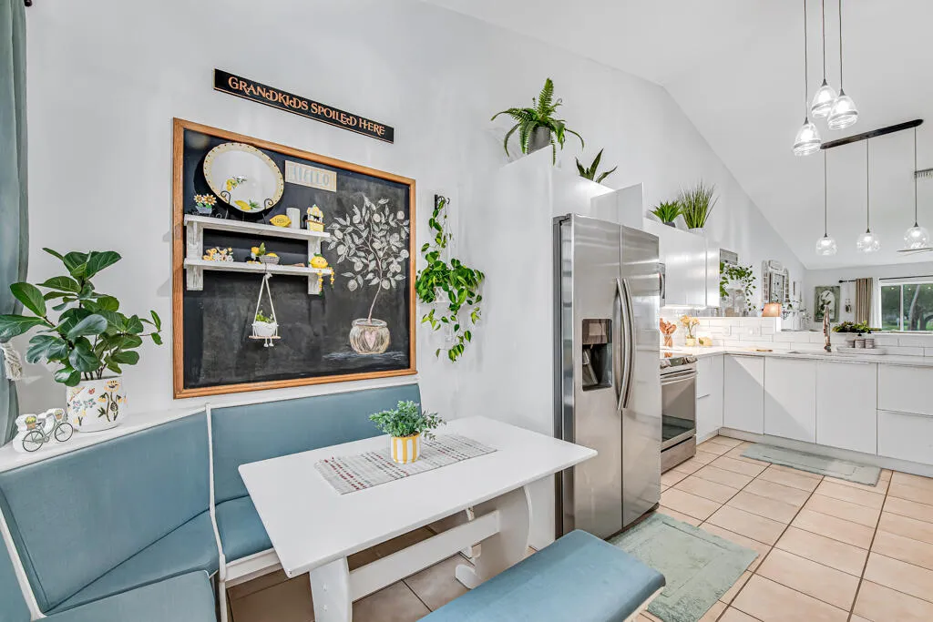 Vaulted ceiling, stainless steel refrigerator, contemporary pendant lighting, white cabinetry, and a subway tile backsplash
