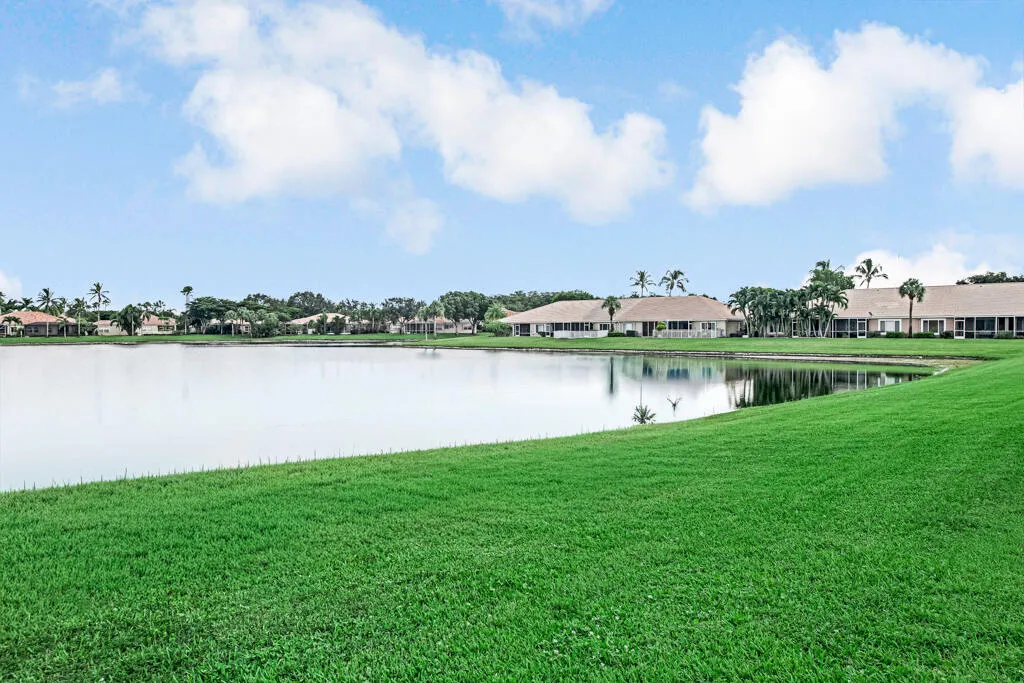 Expansive green lawn bordering a reflective body of water with residential properties in the background