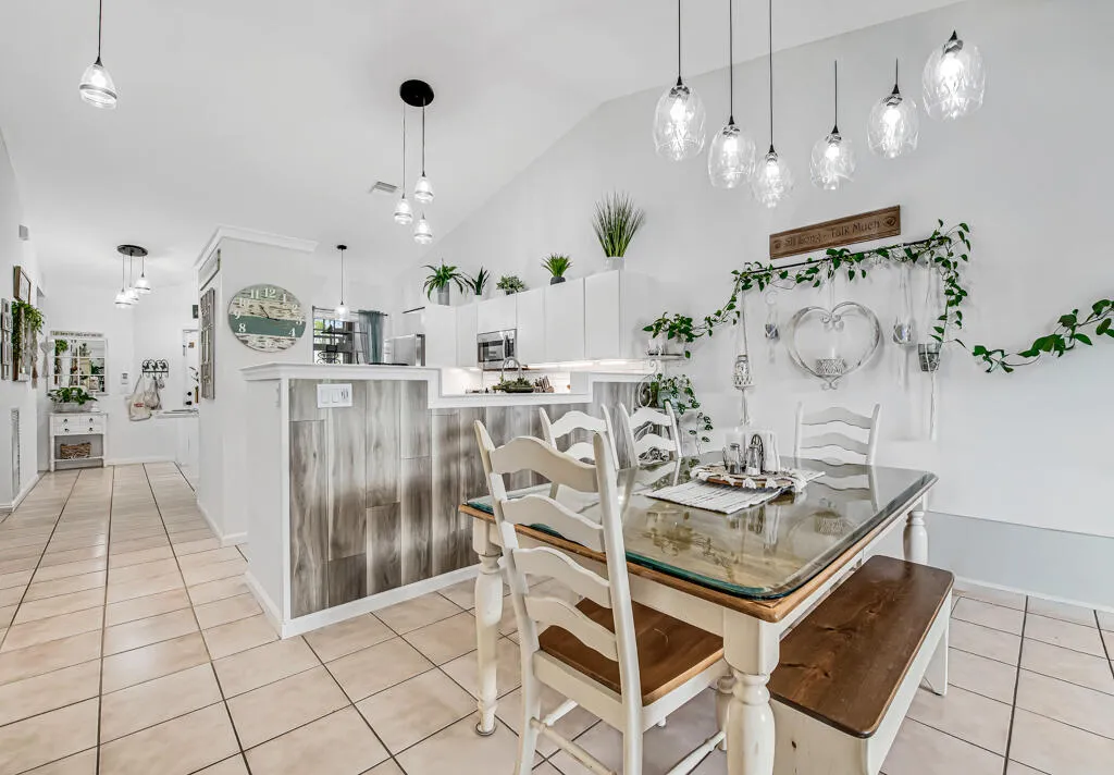 Vaulted white ceiling, tile flooring, pendant lighting, breakfast bar with wood paneling, and white cabinetry