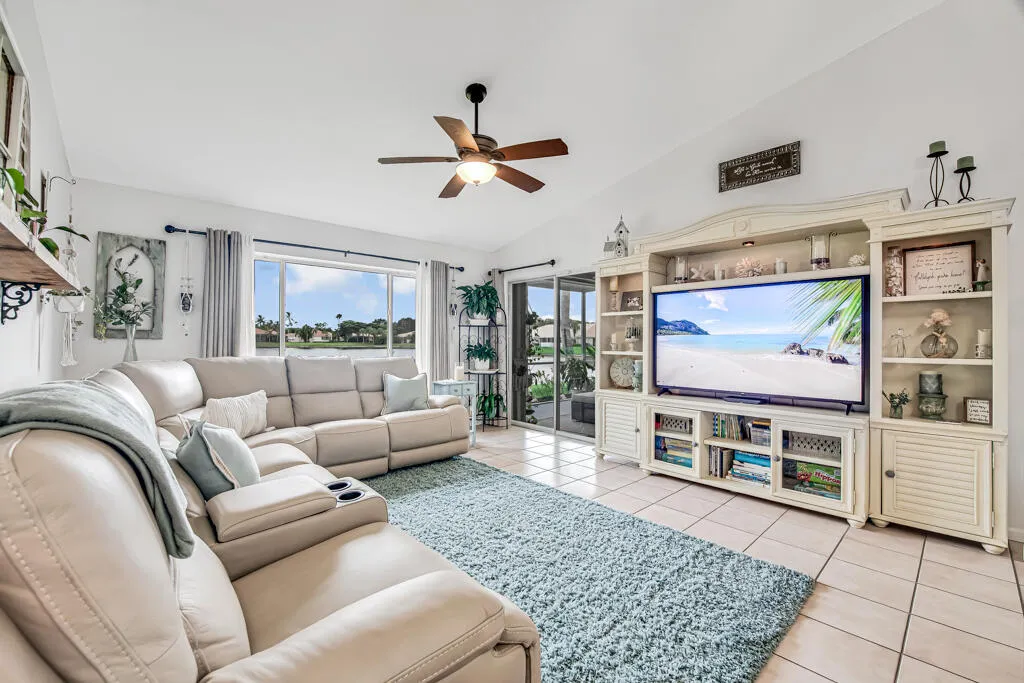 Spacious living area featuring vaulted ceilings, ceiling fan with light, large windows, and tile flooring