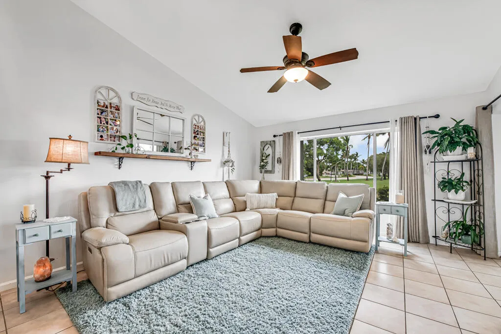 Vaulted ceiling with a ceiling fan, large window overlooking exterior landscaping, and tile flooring
