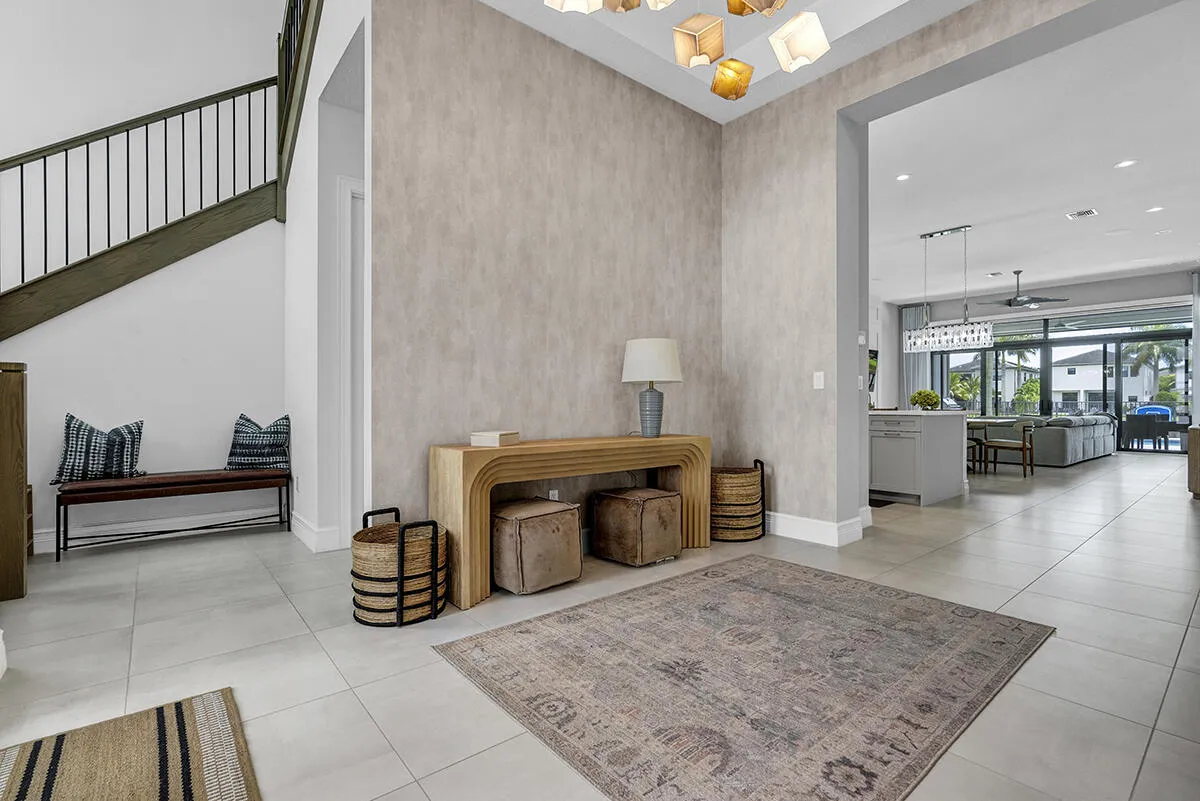 Spacious foyer featuring light-toned tile flooring, a contemporary chandelier, a custom wood staircase with metal balusters, textured wall detailing, and an expansive archway leading to an open-concept interior