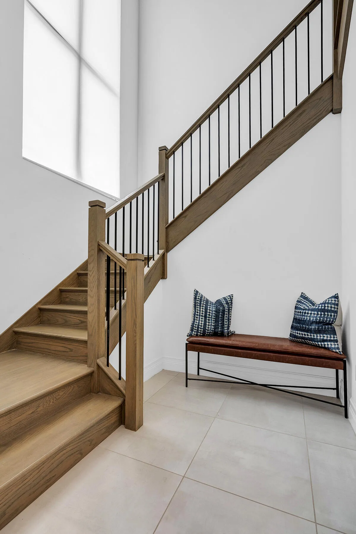 Grand staircase featuring wood-finish treads and risers, a wood-finish handrail, and sleek black metal balusters
