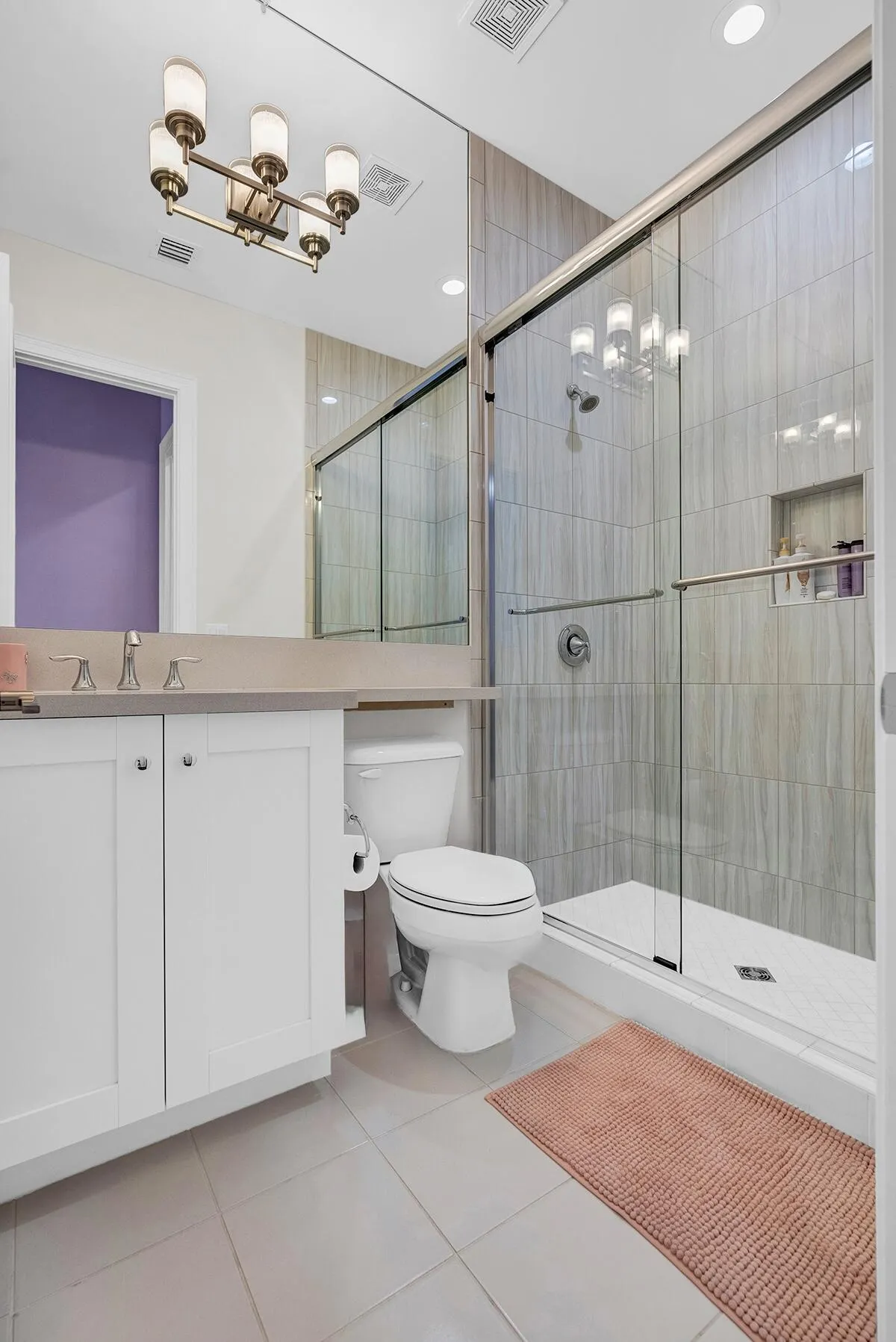 Bathroom featuring a glass-enclosed shower with vertical tile surround and recessed shelving