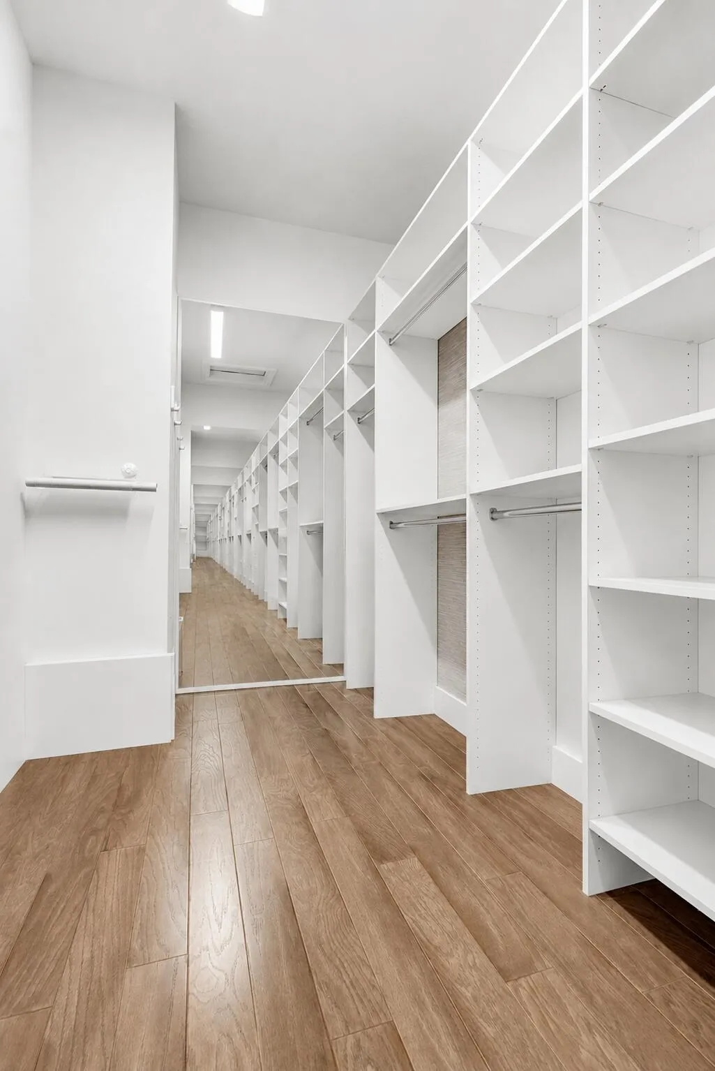 Walk-in closet featuring extensive built-in shelving, hanging rods, light wood-finish flooring, full-length mirror, and recessed lighting
